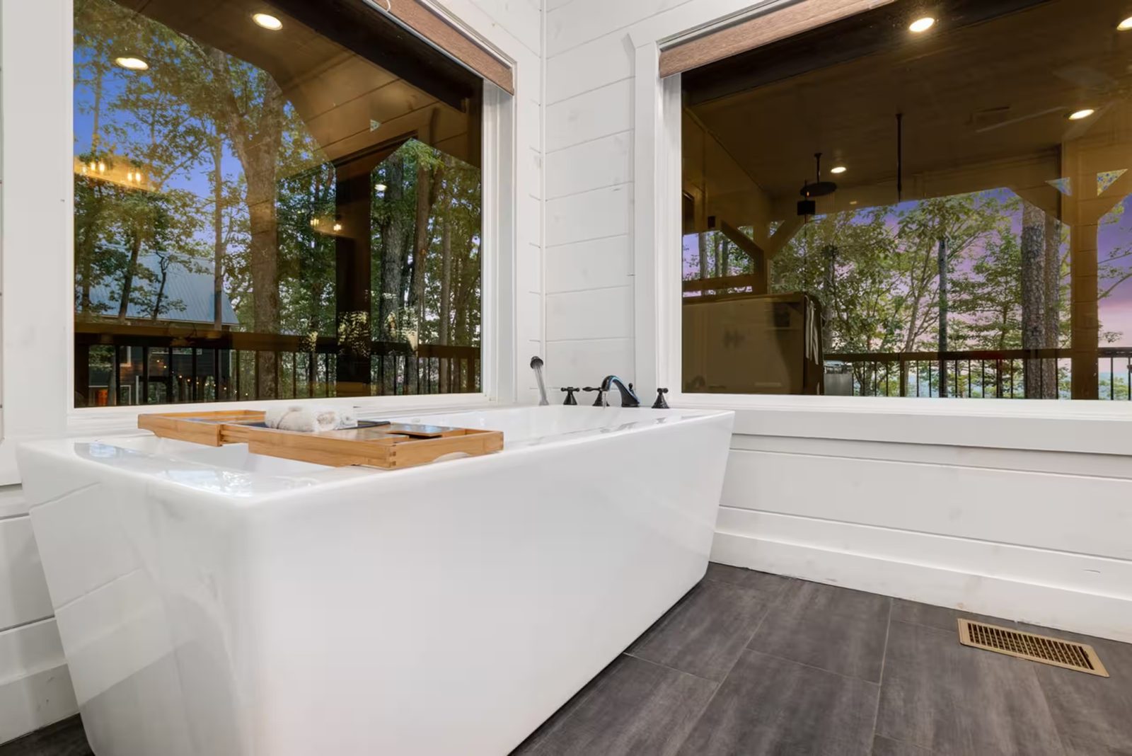Freestanding soaking tub beside windows that look into the trees.