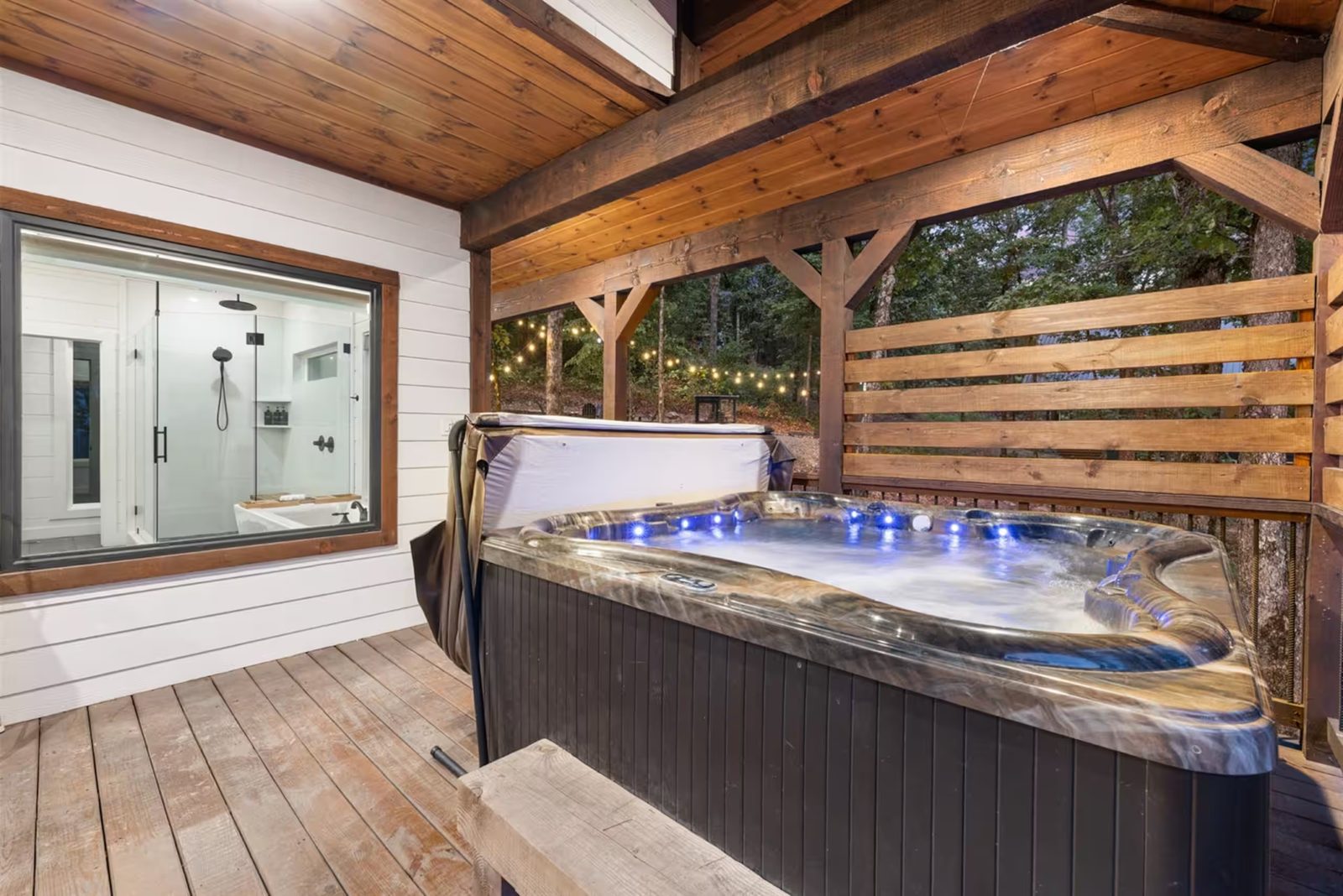 Private hot tub with the cover off, string lights, and a privacy screen.
