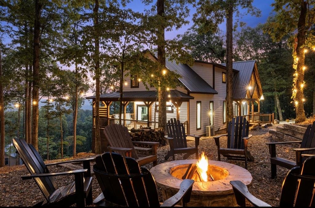 The fire pit lit at dusk, with Adirondack chairs, string lights, and the cabin in the pines.